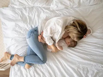 Una mujer da el pecho a su bebé tumbada en la cama Una mujer da el pecho a su bebé tumbada en la cama