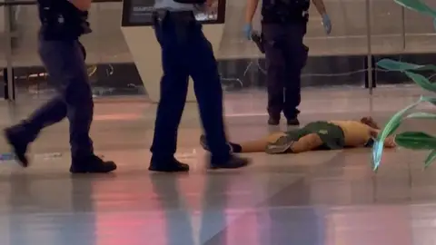 Oficiales de policía caminan junto al cuerpo del atacante que mató a varias personas con un cuchillo en Sidney Oficiales de policía caminan junto al cuerpo del atacante que mató a varias personas con un cuchillo en Sidney