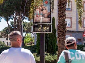 Dos turistas caminan frente a un termómetro que marca los 29 grados de temperatura este sábado en Mahón.