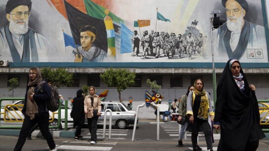 Varias mujeres pasean con el velo por delante de un mural del l&iacute;der supremo iran&iacute;