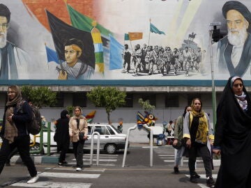 Varias mujeres pasean con el velo por delante de un mural del líder supremo iraní