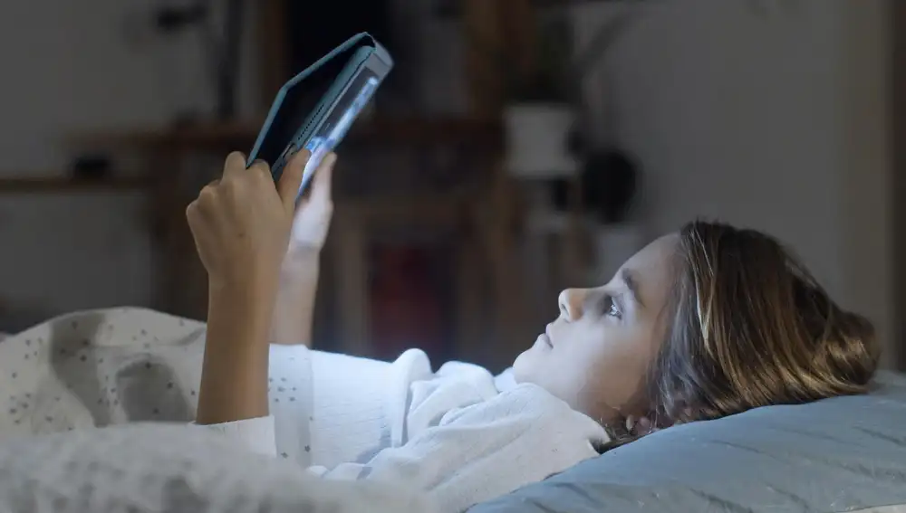 Una niña con una tablet en la cama.