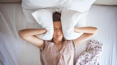 Persona tapándose las orejas con una almohada Persona tapándose las orejas con una almohada