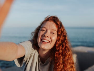 Una chica peliroja sonríe mientras se hace un selfie