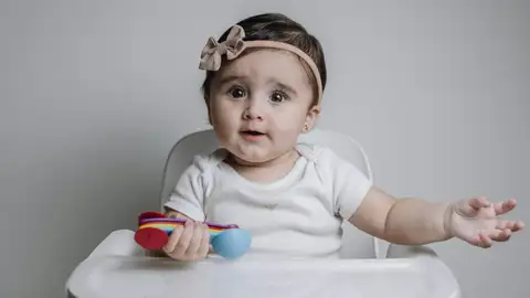 Niña en trona con un juguete en la mano Niña en trona con un juguete en la mano