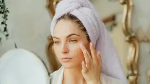 Una mujer se aplica en el rostro productos cosméticos