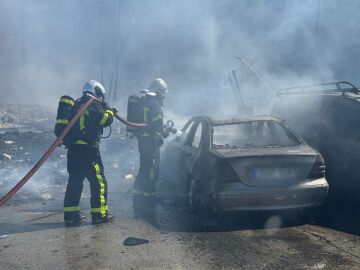 Los bomberos intentan sofocar las llamas de uno de los vehículos calcinados
