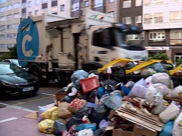 Un camión de la basura de A Coruña pasa por delante de un montón de restos acumulados en los contenedores