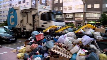 Un camión de la basura de A Coruña pasa por delante de un montón de restos acumulados en los contenedores