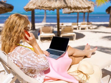 Una mujer trabajando en la playa con el ordenador y el teléfono