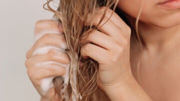 Una mujer aplicándose champú en el pelo