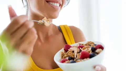Una mujer desayunando un bol de fruta y cereales Una mujer desayunando un bol de fruta y cereales