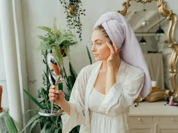 Una mujer con la piel radiante se mira al espejo Una mujer con la piel radiante se mira al espejo