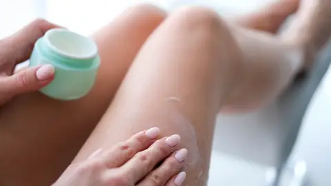 Una persona echándose crema en las piernas Una persona echándose crema en las piernas
