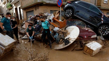 Los vecinos limpian las calles junto a varios coches apilados en Catarroja