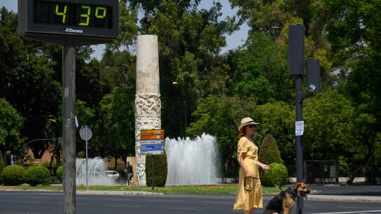 Una mujer pasea a su perro cerca de un term&oacute;metro de Sevilla que marca 43&ordm; C