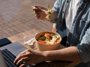 Un hombre comiendo una ensalada frente al ordenador mientras trabaja