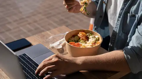 Un hombre comiendo una ensalada frente al ordenador mientras trabaja Un hombre comiendo una ensalada frente al ordenador mientras trabaja