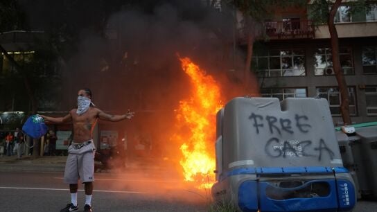 Un contenedor quemado y una persona con la cara tapada en las protestas en favor de Palestina