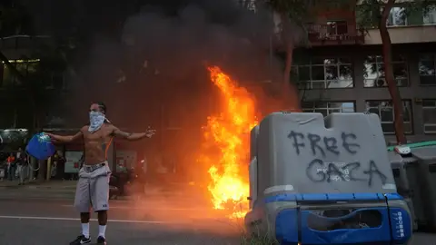 Un contenedor quemado y una persona con la cara tapada en las protestas en favor de Palestina Un contenedor quemado y una persona con la cara tapada en las protestas en favor de Palestina
