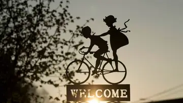 Fotografía de archivo de un cartel de bienvenida con dos personas en una bicicleta Fotografía de archivo de un cartel de bienvenida con dos personas en una bicicleta
