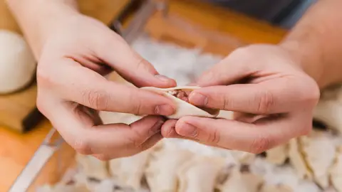 Persona haciendo el pliegue a una gyoza Persona haciendo el pliegue a una gyoza