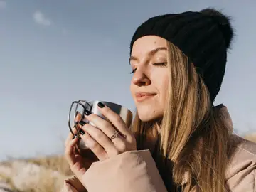 Mujer en invierno con una taza de bebida caliente y frente al sol Mujer en invierno con una taza de bebida caliente y frente al sol
