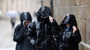 Tres personas protegi&eacute;ndose de la lluvia en Galicia