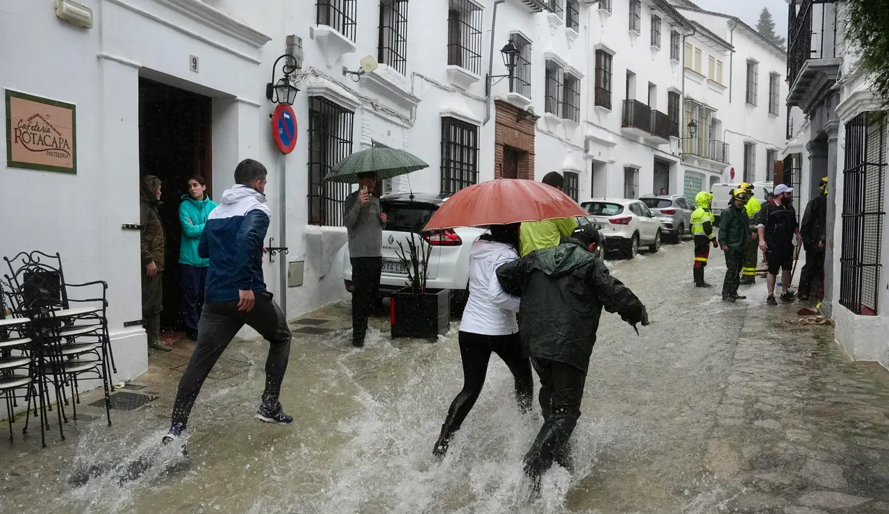 Vecinos de Grazalema corren por una calle inundada debido a las intensas lluvias que se registran este miércoles en la localidad gaditana