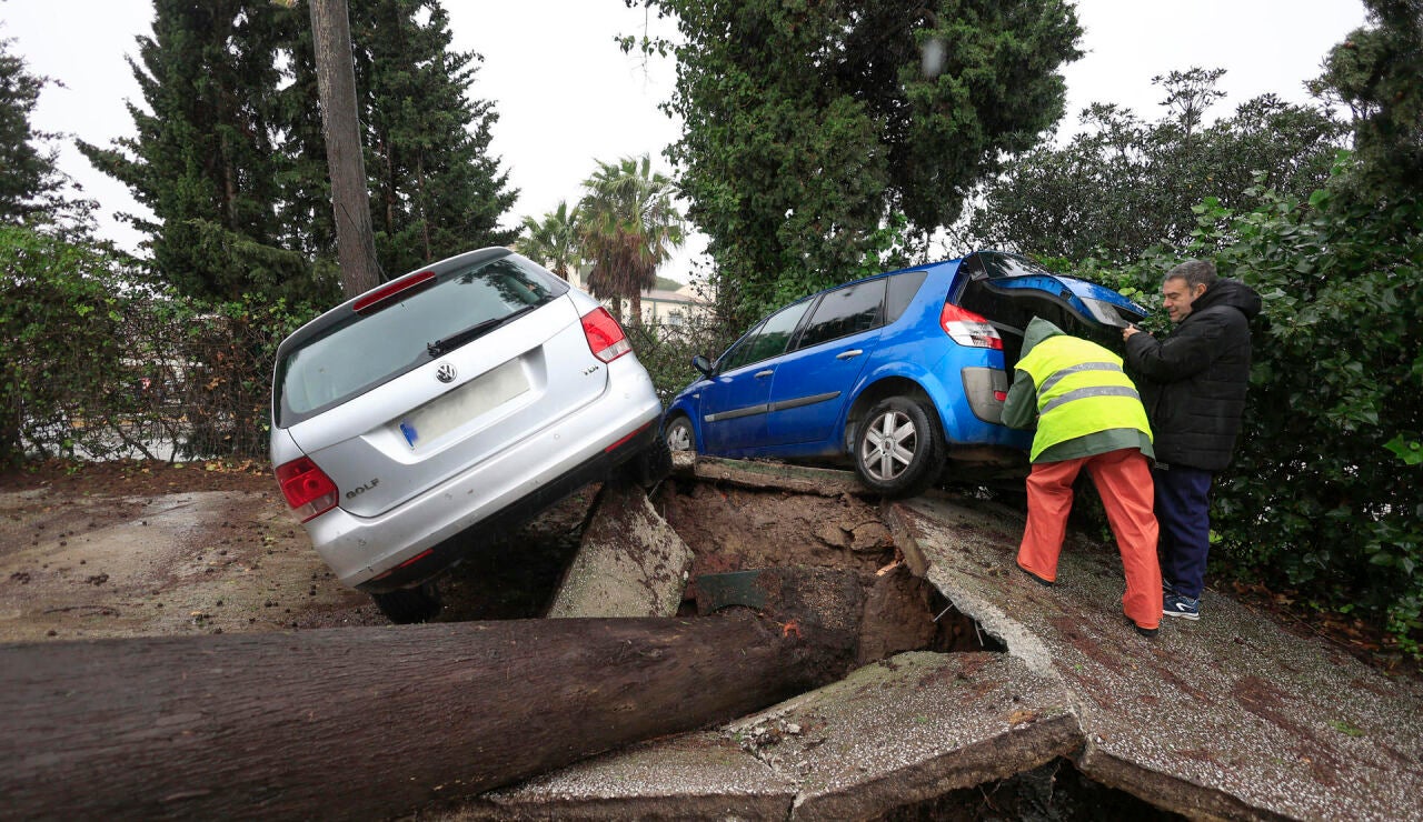 Dos personas junto a unos veh&iacute;culos atrapados al levantarse el pavimento tras caerse un &aacute;rbol este mi&eacute;rcoles en Los Barrios (C&aacute;diz), debido al fuerte temporal de levante que azota la zona del Campo de Gibraltar