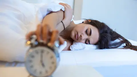 Mujer dormida en la cama apaga el despertador Mujer dormida en la cama apaga el despertador