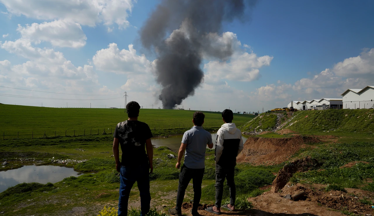 Personas observan humo elevándose desde un depósito de aceite de motor en las afueras de Erbil, después de que fuera alcanzado por un ataque con drones.