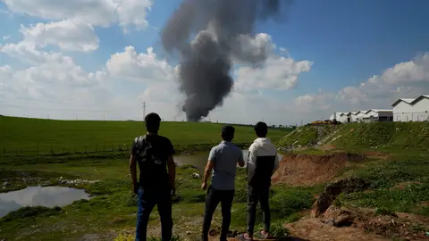 Personas observan humo elevándose desde un depósito de aceite de motor en las afueras de Erbil, después de que fuera alcanzado por un ataque con drones. Personas observan humo elevándose desde un depósito de aceite de motor en las afueras de Erbil, después de que fuera alcanzado por un ataque con drones.