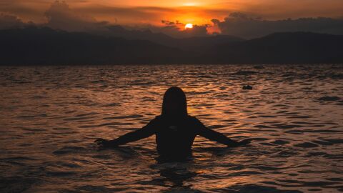 Mujer bañándose en la playa durante la puesta de sol 
