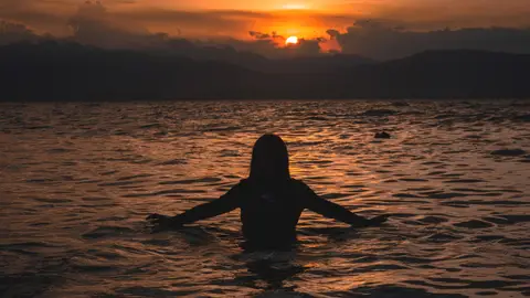 Mujer bañándose en la playa durante la puesta de sol Mujer bañándose en la playa durante la puesta de sol