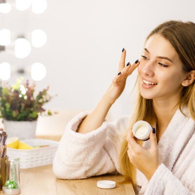 Mujer poni&eacute;ndose cosm&eacute;tico y mir&aacute;ndose al espejo 
