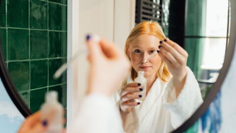 Mujer con un cosmético en la mano frente a un espejo