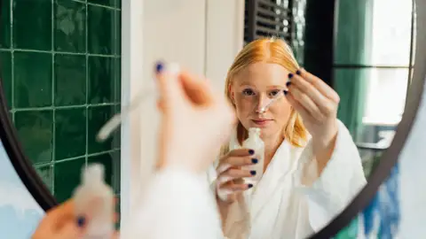 Mujer con un cosmético en la mano frente a un espejo Mujer con un cosmético en la mano frente a un espejo