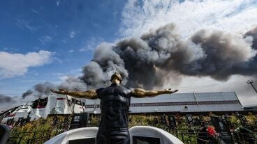 Imagen de una escultura funeraria en un cementerio mientras el humo se eleva sobre una instalaci&oacute;n de Wildberries 