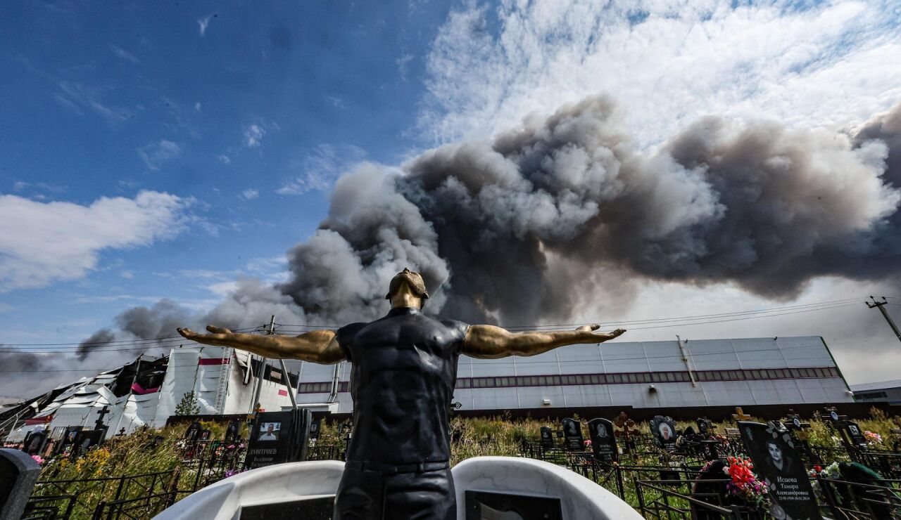 Imagen de una escultura funeraria en un cementerio mientras el humo se eleva sobre una instalaci&oacute;n de Wildberries 