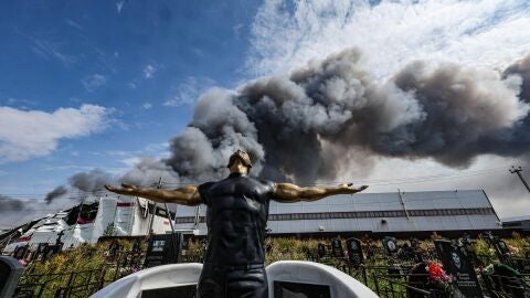 Imagen de una escultura funeraria en un cementerio mientras el humo se eleva sobre una instalaci&oacute;n de Wildberries 