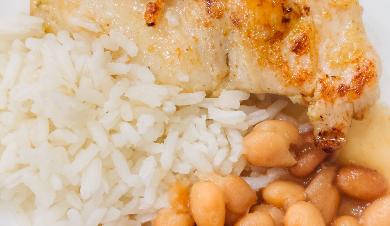 Primer plano de un delicioso pollo a la parrilla servido con arroz y frijoles en un plato.